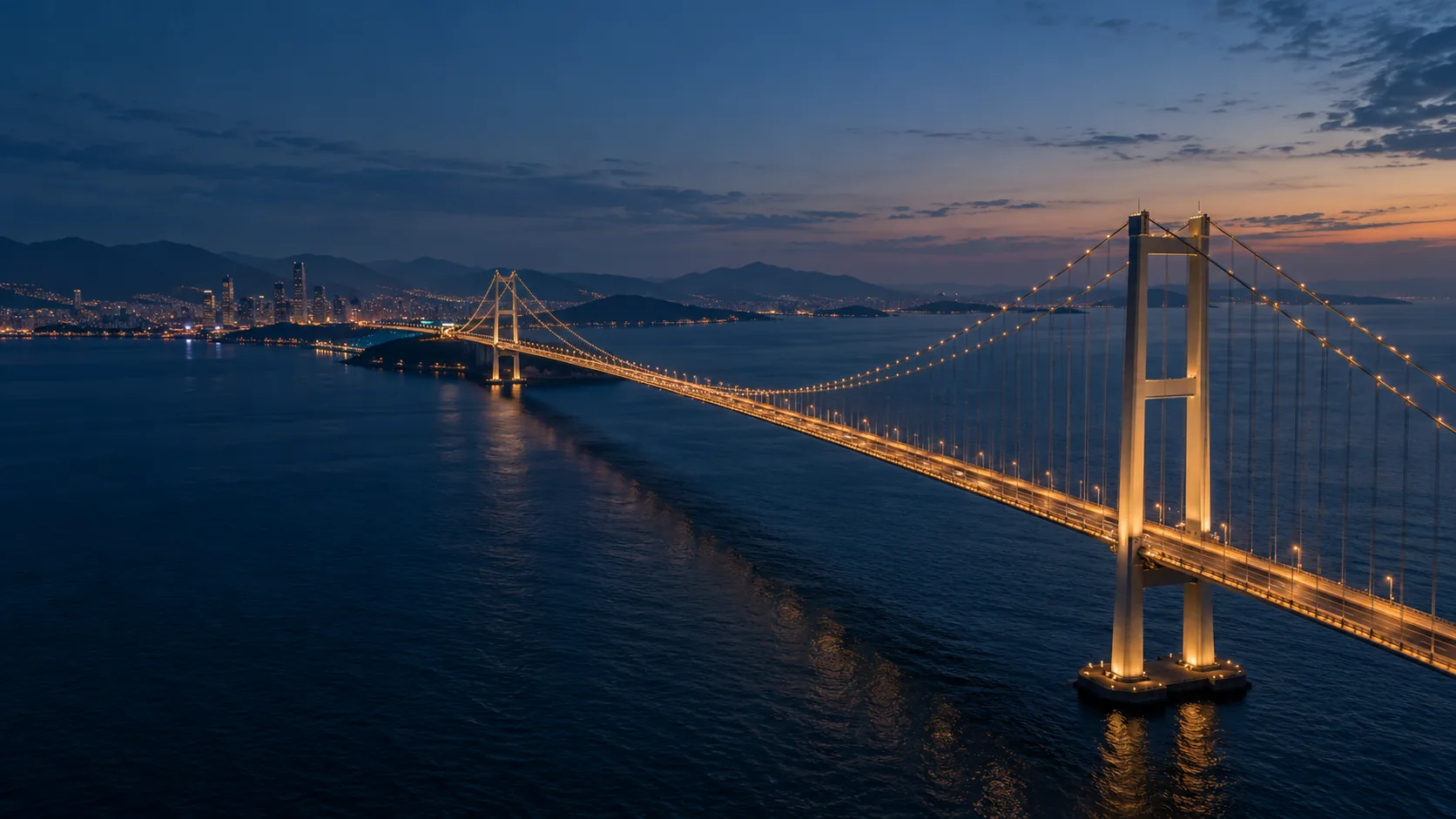 An illuminated bridge crossing blue coastal water.